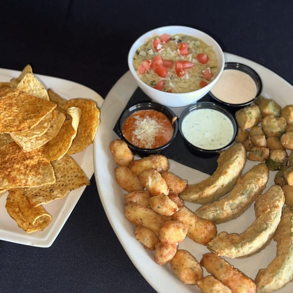 A platter of fried appetizers including avocado, okra, cheese curds, dips, and a side of tortilla chips.