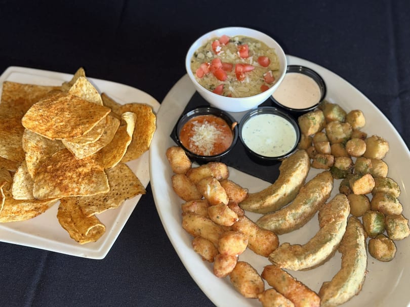 A platter of fried appetizers including avocado, okra, cheese curds, dips, and a side of tortilla chips.