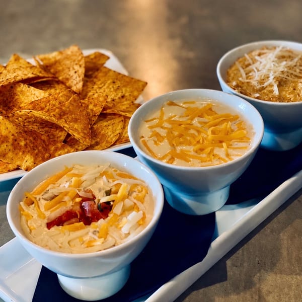 A trio of warm dips with shredded cheese served alongside crispy tortilla chips.