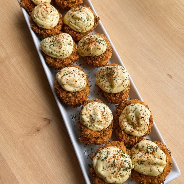 Deep fried deviled eggs topped with creamy filling and seasoning, arranged on a white platter.