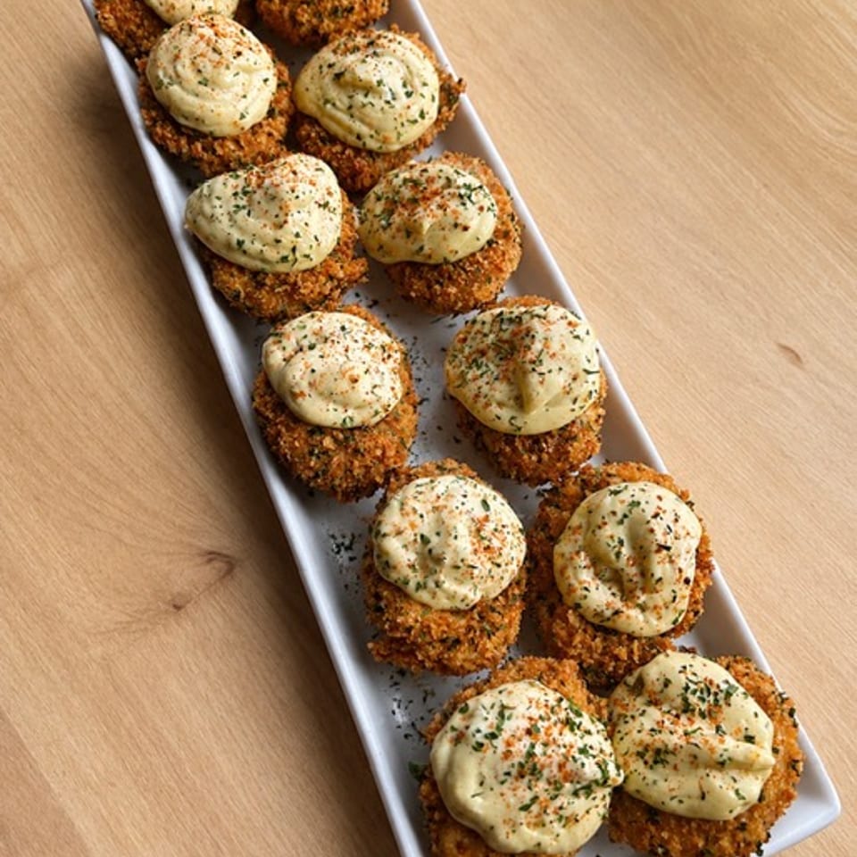 Deep fried deviled eggs topped with creamy filling and seasoning, arranged on a white platter.
