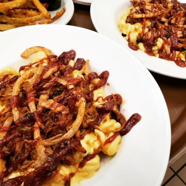 Two plates of macaroni and cheese topped with pulled pork, BBQ sauce and crispy fried onions.