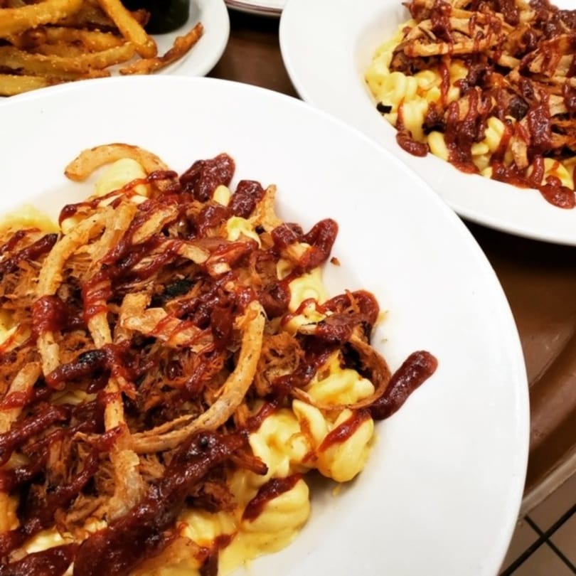 Two plates of macaroni and cheese topped with pulled pork, BBQ sauce, and crispy fried onions.