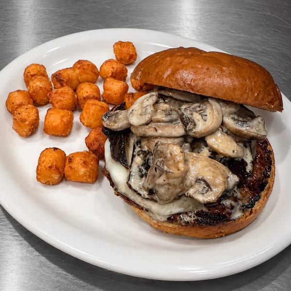 Mushroom and cheese burger with a side of crispy tater tots on a white plate.