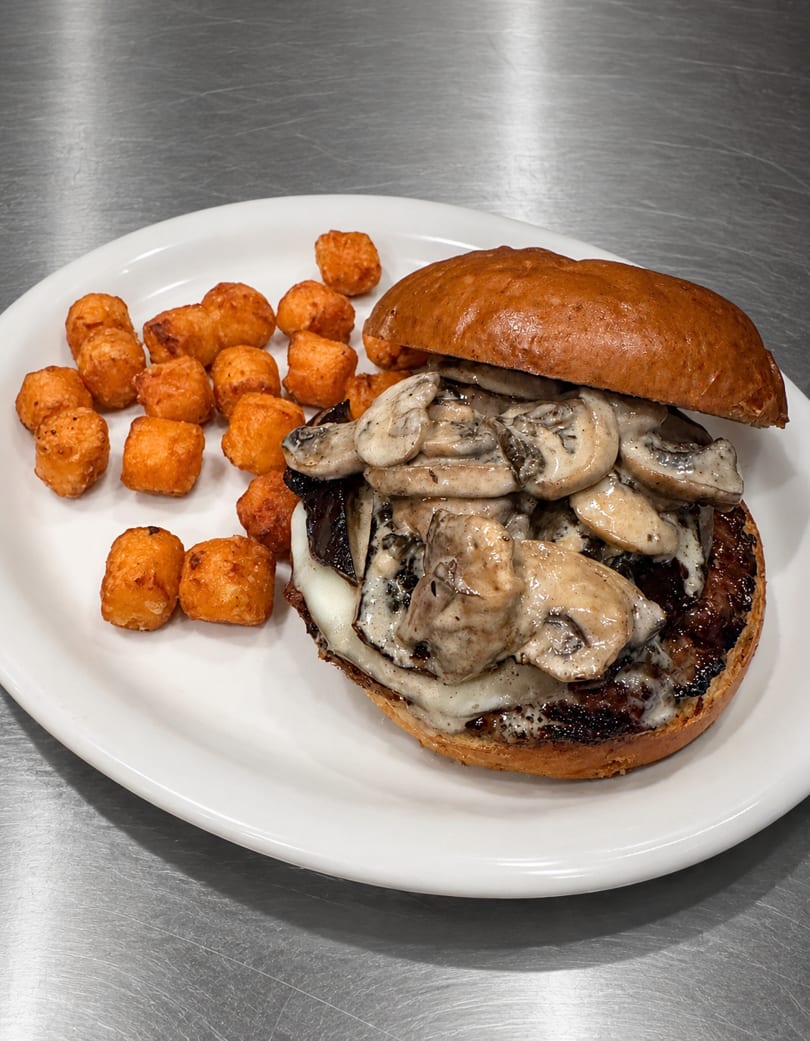 Mushroom and cheese burger with a side of crispy tater tots on a white plate.