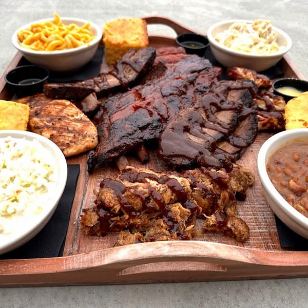 Large barbecue platter with ribs, pulled pork, chicken, mac and cheese, coleslaw, baked beans, and cornbread.