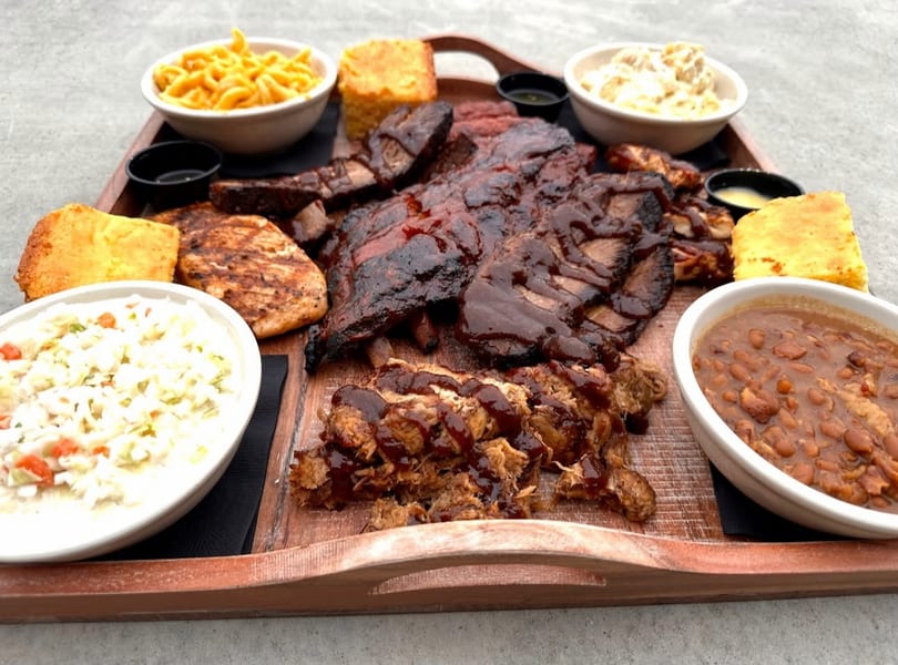 Large barbecue platter with ribs, pulled pork, chicken, mac and cheese, coleslaw, baked beans, and cornbread.