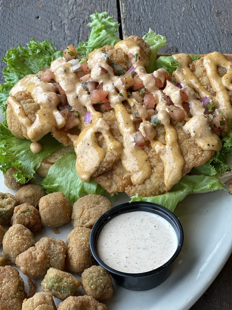 Fried chicken sandwich with lettuce, pico de gallo, and sauce, served with fried okra and ranch.