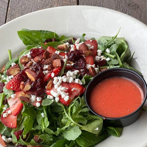 A fresh salad with strawberries, feta, almonds and cranberries, served with a side of dressing.