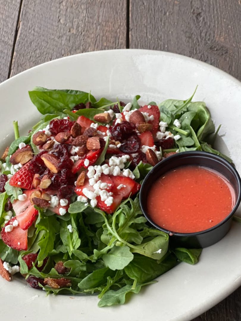 A fresh salad with strawberries, feta, almonds, and cranberries, served with a side of dressing.