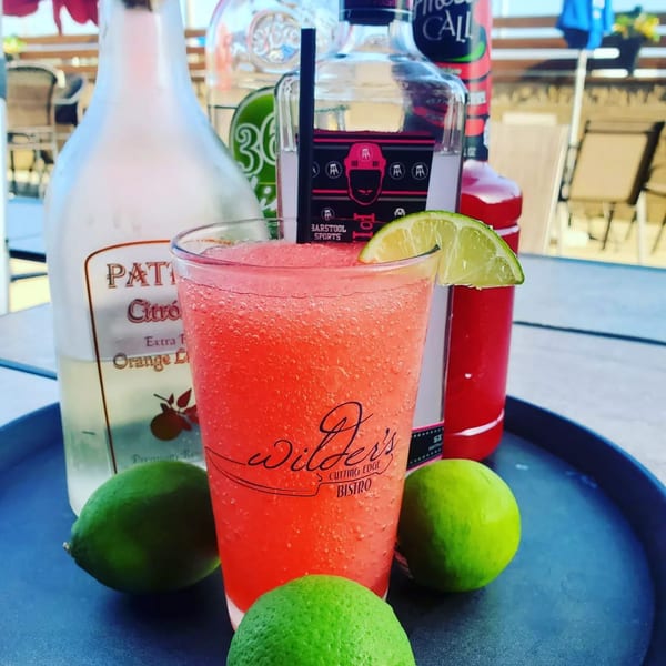 A branded Wilder's frozen cocktail garnished with lime, surrounded by fresh limes on a tray with premium liquor bottles.