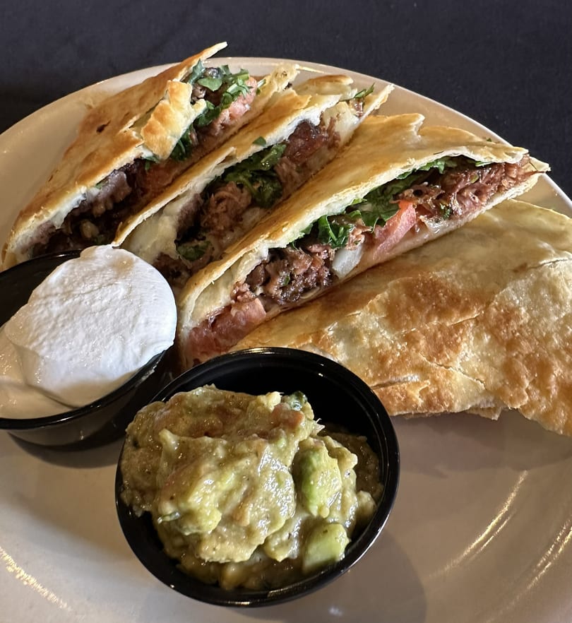 Beef quesadillas with cilantro, tomatoes, and onions, served with guacamole and sour cream.