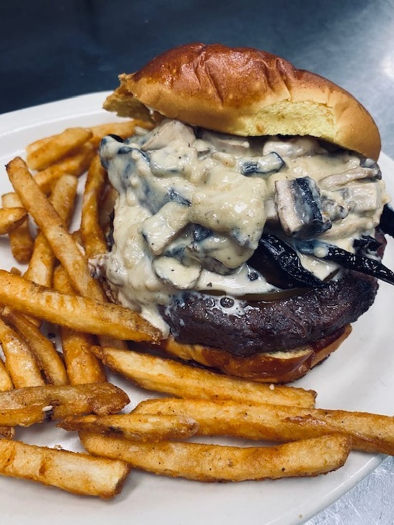 Gourmet burger with creamy mushroom sauce and crispy fries on a white plate.